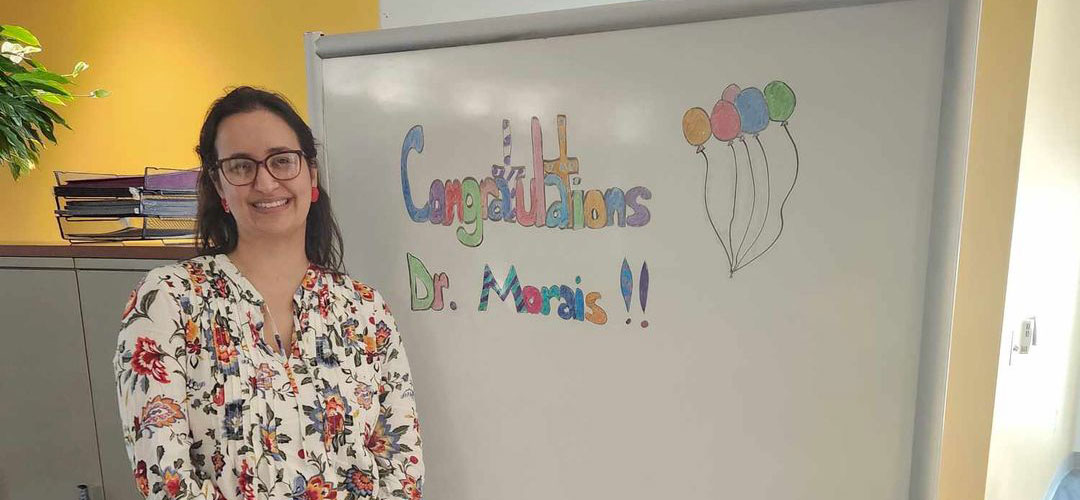 Dr. Morais poses in front of a "Congratulations" message, written on a white board.