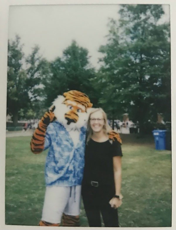 A person poses with a tiger mascot outdoors.