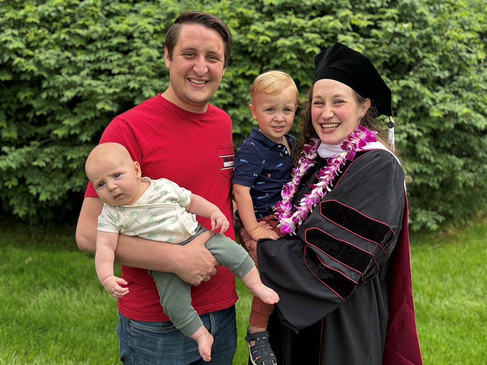 A family poses outdoors with a graduate in regalia.